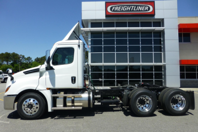 White Freightliner Cascadia day cab truck in front of dealership building showing cab, chassis, and rear axles with dual rear wheels.