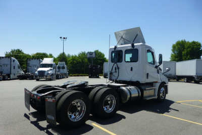 Freightliner Cascadia day cab truck rear-left view showing dual rear axles and raised cab hood in parking lot.