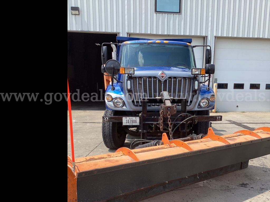 International 7300 truck in front of a building with a large orange plow blade attachment.