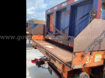 Flatbed truck bed with orange and blue equipment; visible labels include 'CAUTION' sticker, '37' and weathered markings; chain and rust protective edges.
