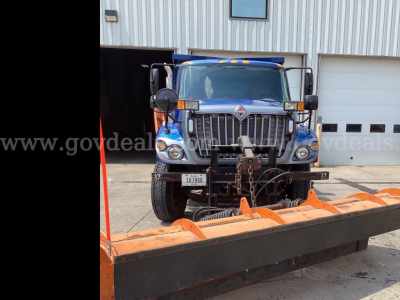 International 7300 truck in front of a building with a large orange plow blade attachment.