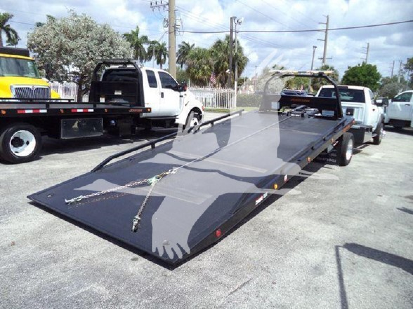 Ram 5500 rollback flatbed truck in a parking lot with a black hydraulic tilt deck and winch points visible.