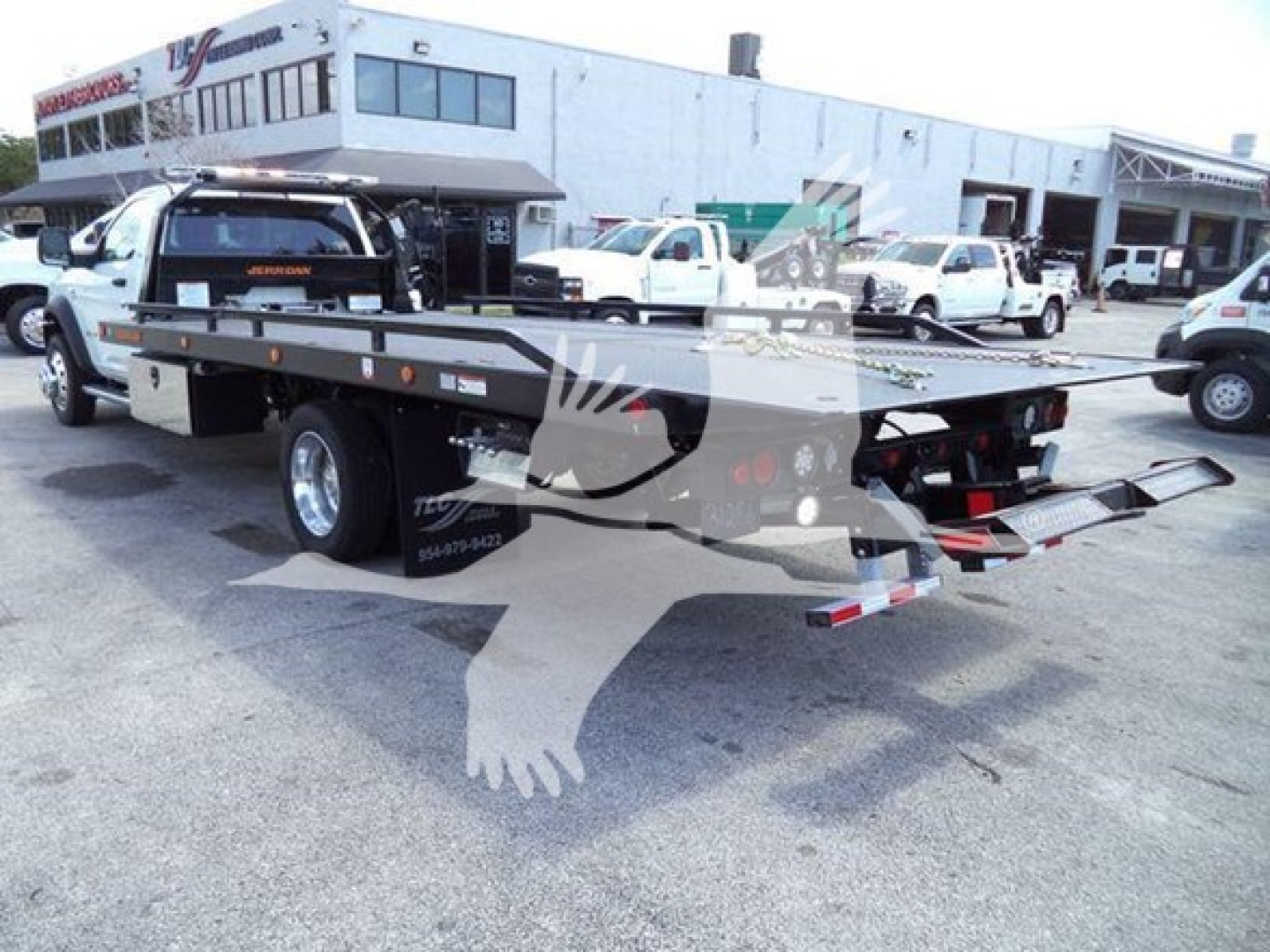 Ram 5500 rollback tow truck flatbed with dual rear ramps and hydraulic lift, white color, dealership lot in background, visible stock number J40687.