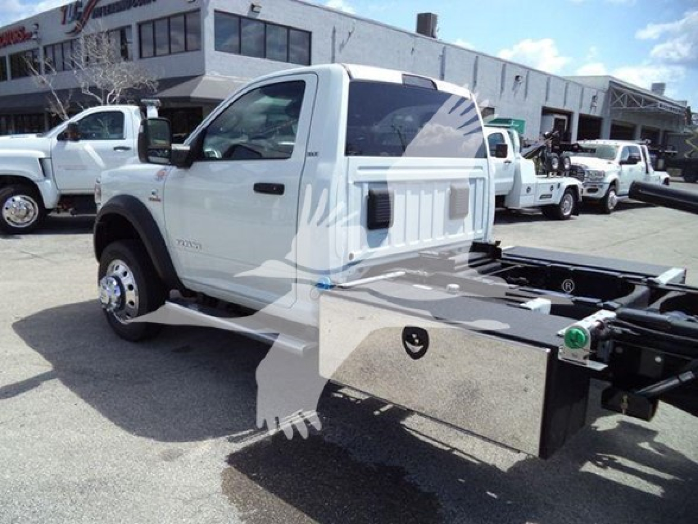 Ram 5500 rollback truck cab rear view showing chassis and hitch assembly with white body and dealership lot in background.