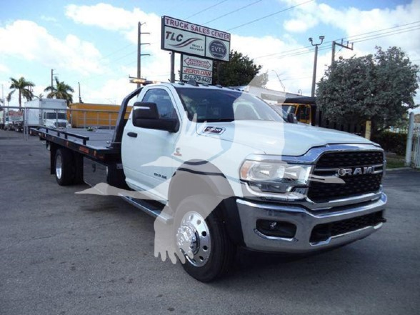 Ram 5500 rollback tow truck front-right view showing RAM grille, headlights, and flatbed; TLC Truck Sales Center sign in background.