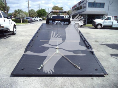 Ram 5500 rollback bed with hydraulic tow wheel, front of flatbed shows cleats and chains, dealership lot in background.