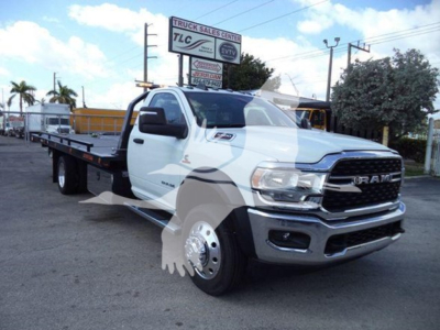 Ram 5500 rollback tow truck front-right view showing RAM grille, headlights, and flatbed; TLC Truck Sales Center sign in background.
