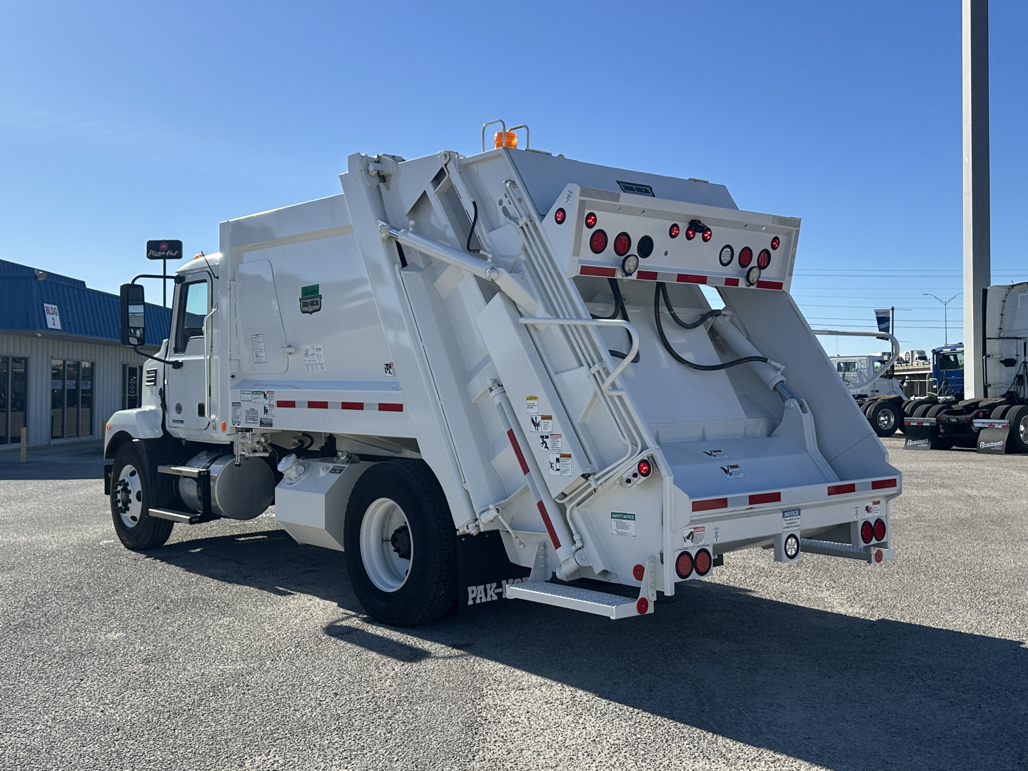 Mack MD6 refuse truck body side and rear view showing lift system and rear hopper with hydraulic components and warning lights.