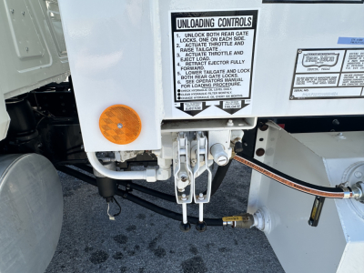 Front hitch area of a 2026 Mack MD6 refuse truck showing unl towing/controls label and hitch mechanism with hoses and metal brackets.