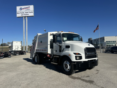 Mack MD6 refuse truck in a dealership lot, front view showing cab and body with a Brackett's sign in background.