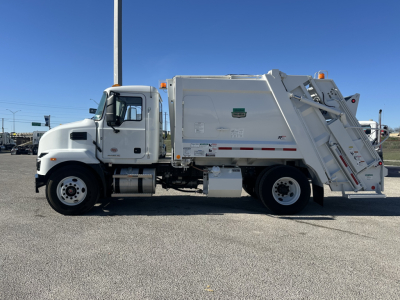 Truck side view of a white Mack MD6 refuse truck showing cab and rear compactor body with warning decals and reflective tape.