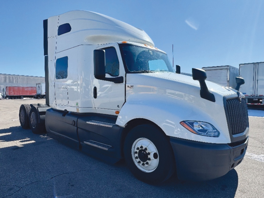 Truck cab in-view showing International LT625 sleeper tractor with white paint and large grille, front-right perspective.