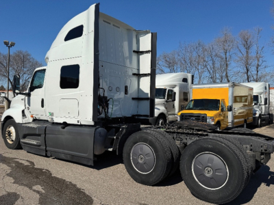 Truck tractor in side view showing LT625 sleeper cab with white paint and black chassis. Dual rear axles, fifth wheel area visible, other trucks in background.
