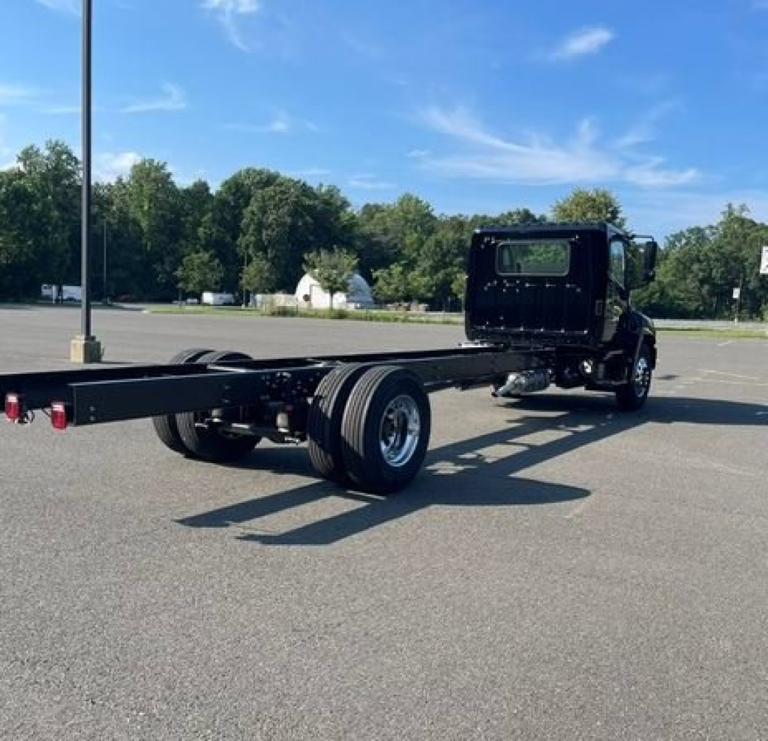 Truck chassis showing rear view of cab and long flatbed frame with dual rear axles and attached suspension.