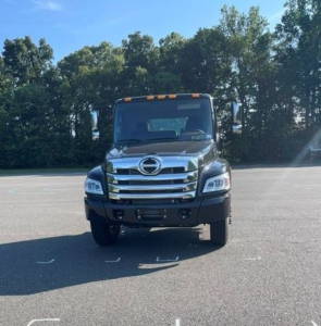 Front view of a new 2027 Hino L7 cab chassis truck in a parking lot showing chrome grille, Hino emblem, and large headlights.