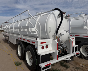 Flatbed trailer with a large white vacuum steel tank, side rails, and rear equipment. Text not clearly legible; visible features include circular manhole and hoses.