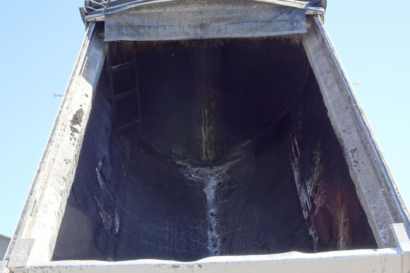 Dump truck bed opening with blackened interior in-service shows metal sides and tailgate edge.