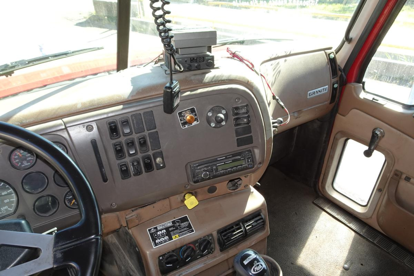 Dashboard and cabin interior of a Mack CV (Granite) truck showing steering wheel, control panel, radio, gauges, and grab handles.