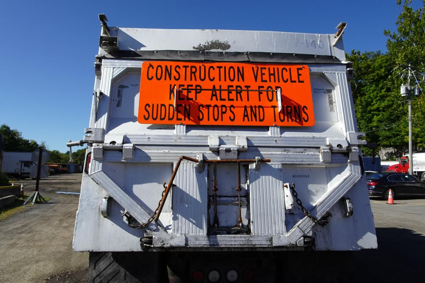 Back view of a Mack CV Granite dump truck with an orange construction vehicle sign on the tailgate.