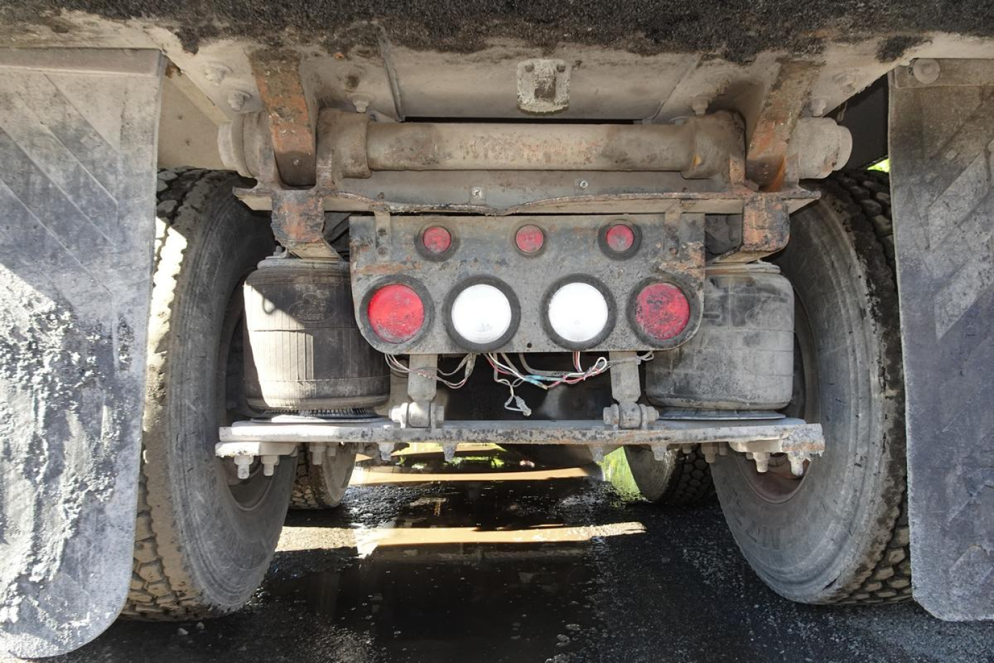 Mack CV Granite dump truck rear view showing differential, frame, and twin rear wheels with hydraulic lines and red/white warning lights at center.