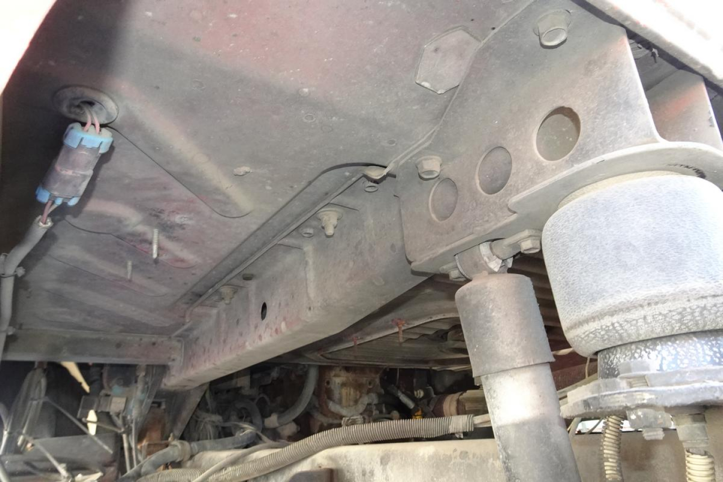 Underbody view of a Mack CV (Granite) CV713 dump truck showing chassis, suspension components, hoses, and wiring harnesses.
