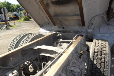 Dump truck chassis with raised cargo bed showing suspension, dual rear wheels, and undercarriage components.
