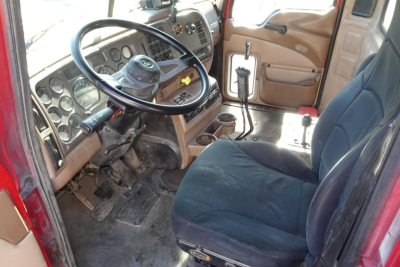 Cab interior of a 2005 Mack CV Granite CV713 dump truck showing steering wheel, dashboard, pedals, gear lever, and front seats.