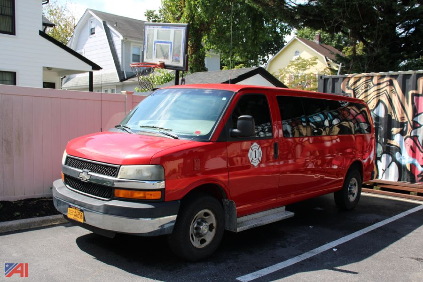 Red 2008 Chevrolet Express passenger van in a parking lot showing side and front view with graffiti mural on fence