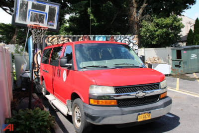 Chevrolet Express van with red exterior, front view in a parking lot, showing passenger van profile and front grille
