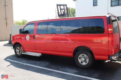 Red Chevrolet Express passenger van in profile view with black-tinted windows and running boards.