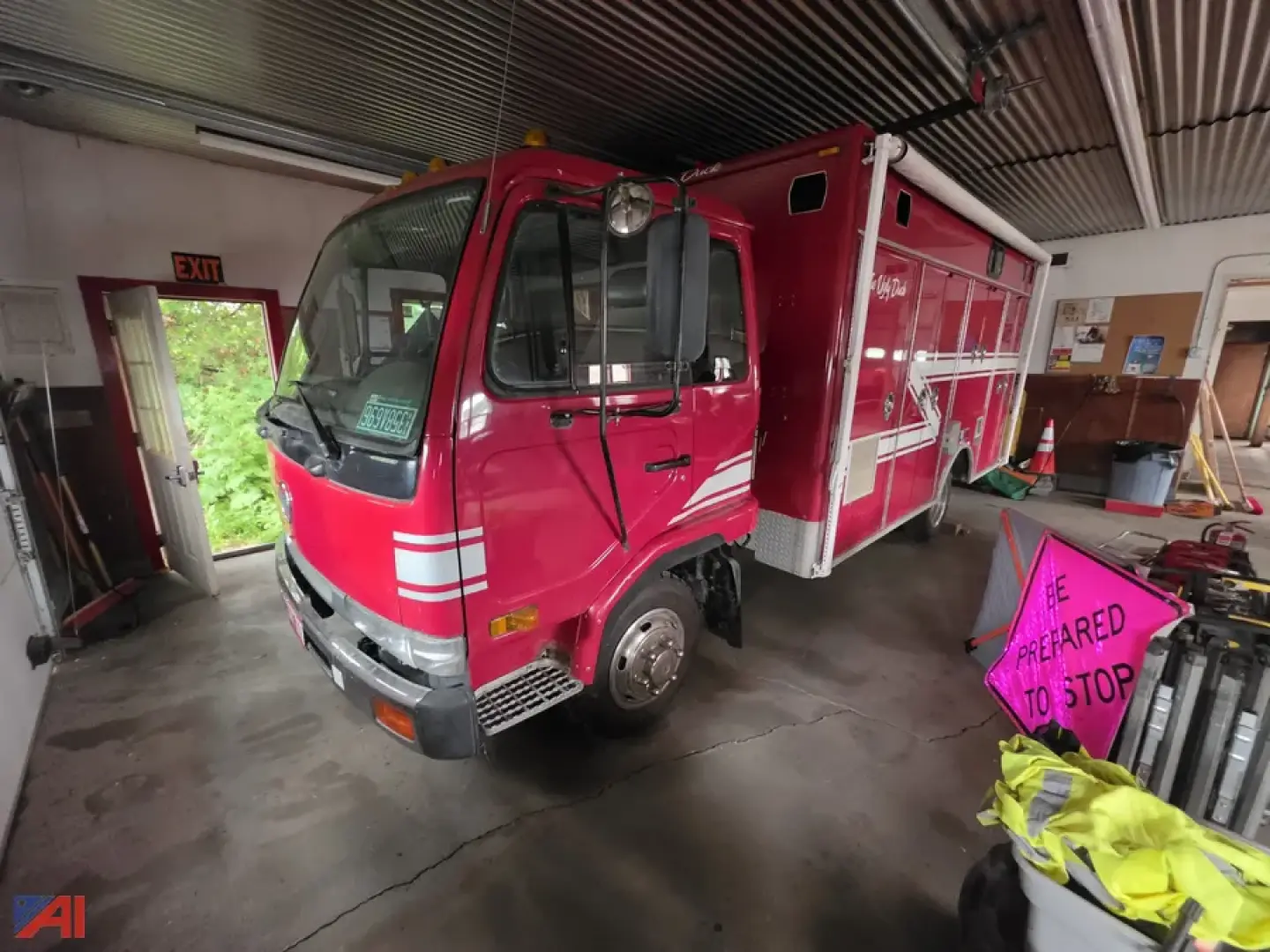 Fire rescue truck cab and body in a garage; pink/red Nissan UD 1800 rescue vehicle with equipment compartments along the side.