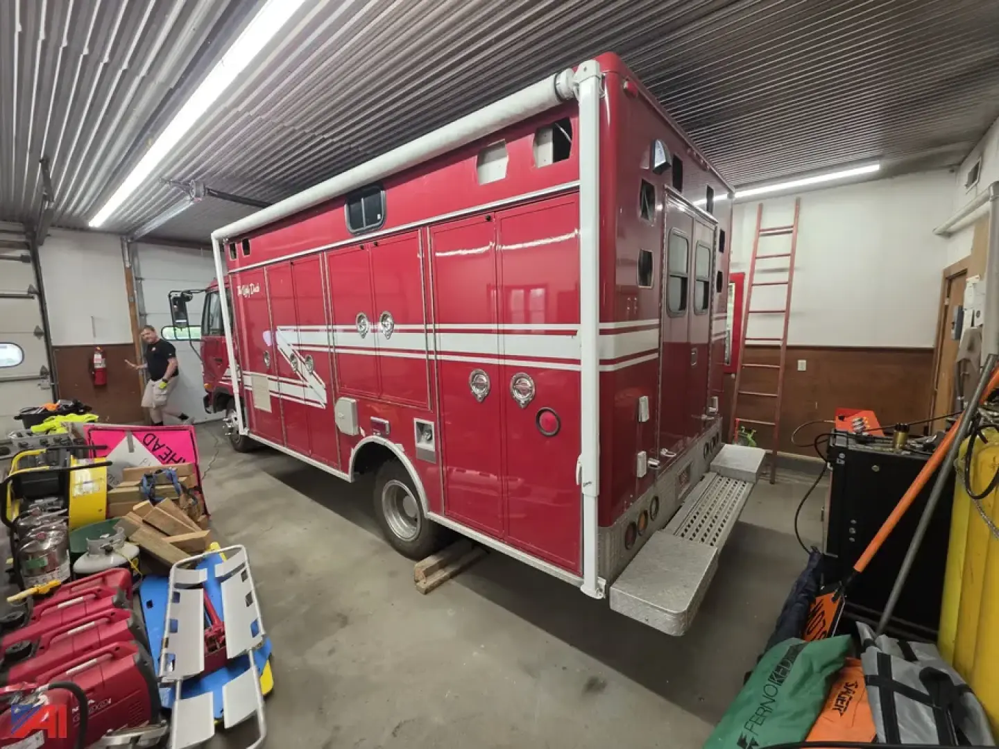 Red Nissan UD 1800 rescue truck in a workshop with equipment around, side compartments and ladder visible.