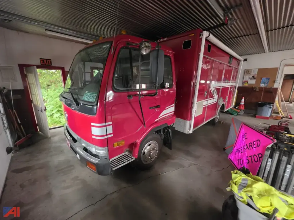 Fire rescue truck cab and body in a garage; pink/red Nissan UD 1800 rescue vehicle with equipment compartments along the side.