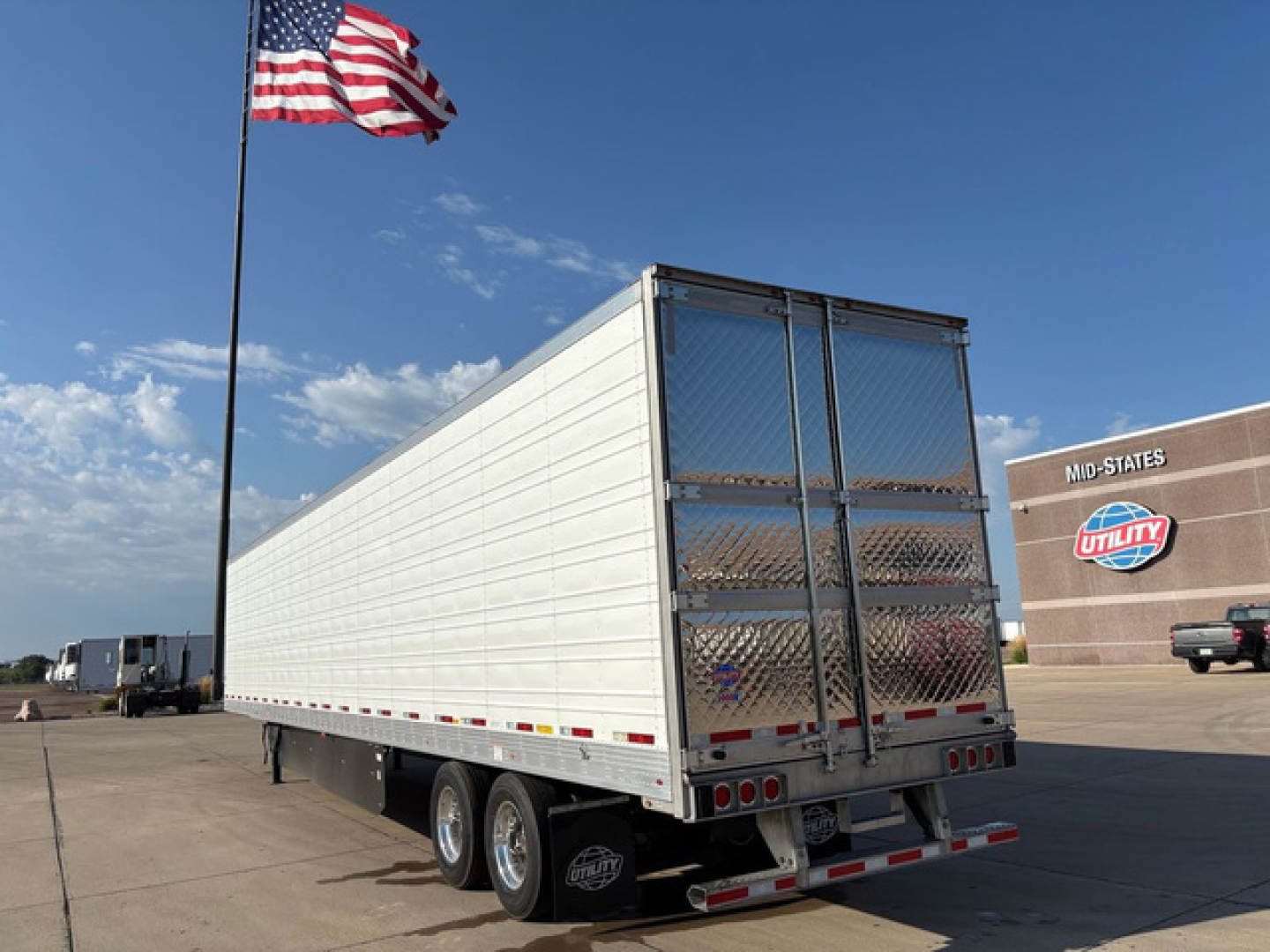 Trailer side and rear view of a new 2027 utility refrigerated trailer with aluminum exterior, dual rear doors, triple axle setup, and reflective safety stripes.