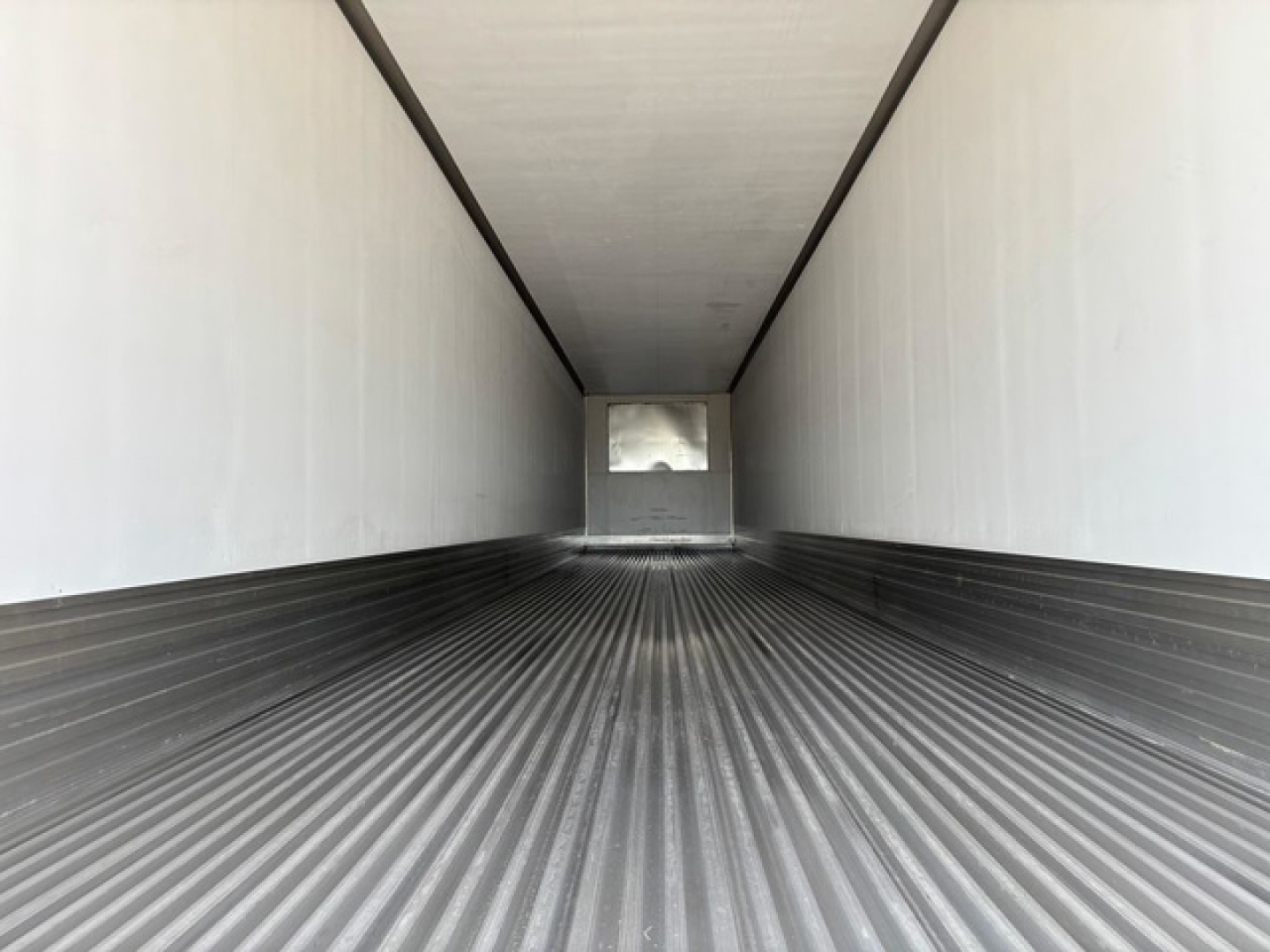 Trailer interior showing long empty refrigerated box with ribbed floor and white walls, view toward rear doors.