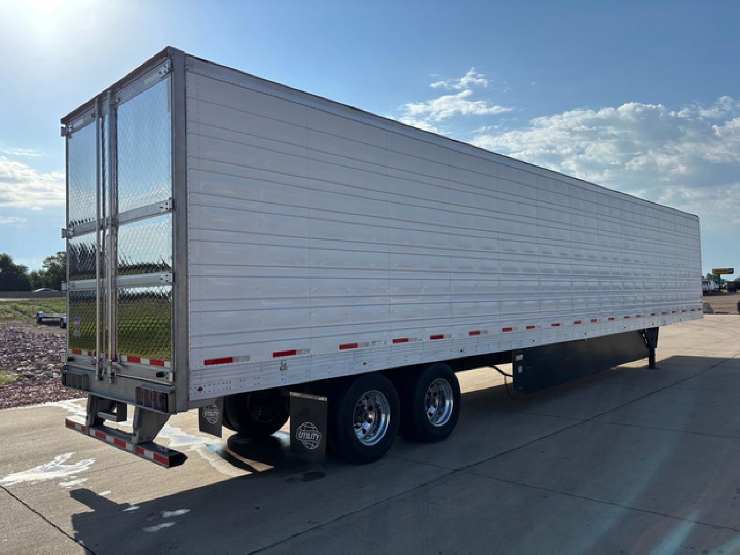 Utility reefer trailer showing aluminum side panels, tandem axles, rear doors, and chrome wheels under clear sky.