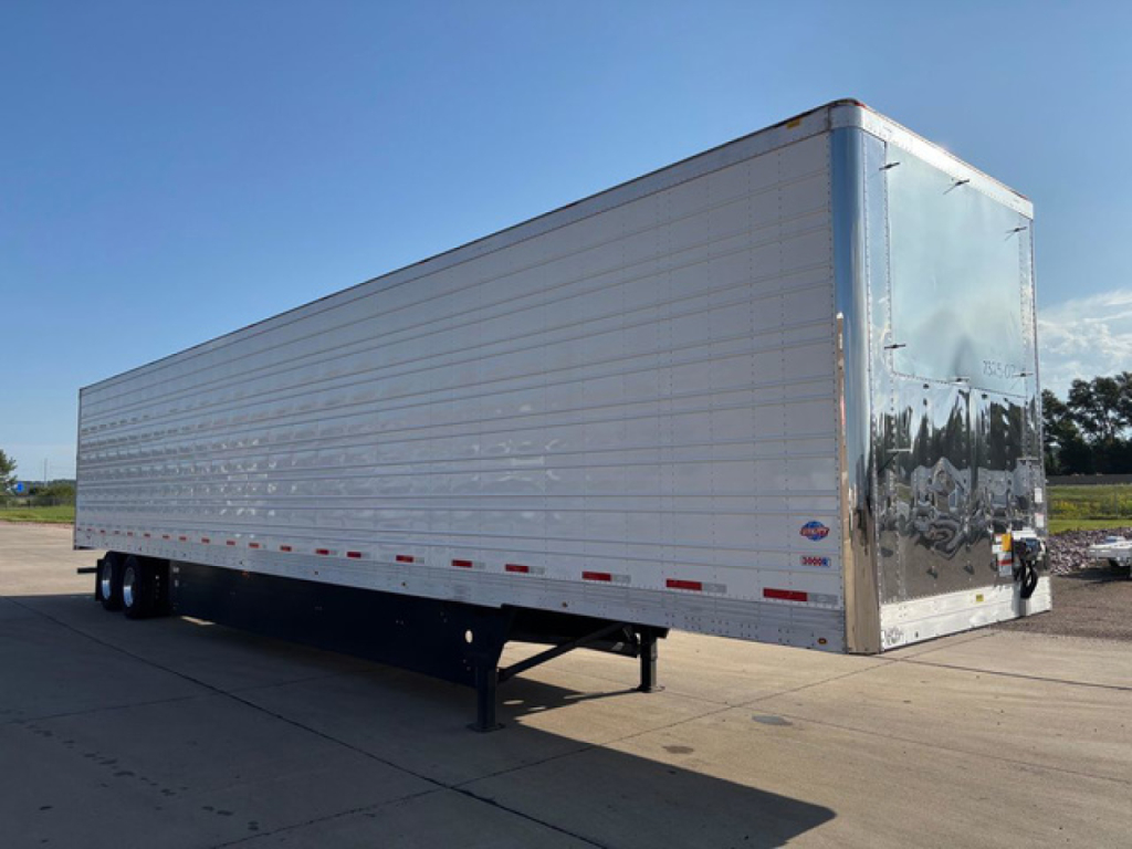 2027 Utility Reefer trailer on trailer parking area showing side and rear. Refrigerated box with silver exterior and tandem rear axles, landing gear at front.