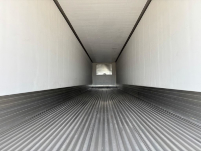 Trailer interior showing long empty refrigerated box with ribbed floor and white walls, view toward rear doors.