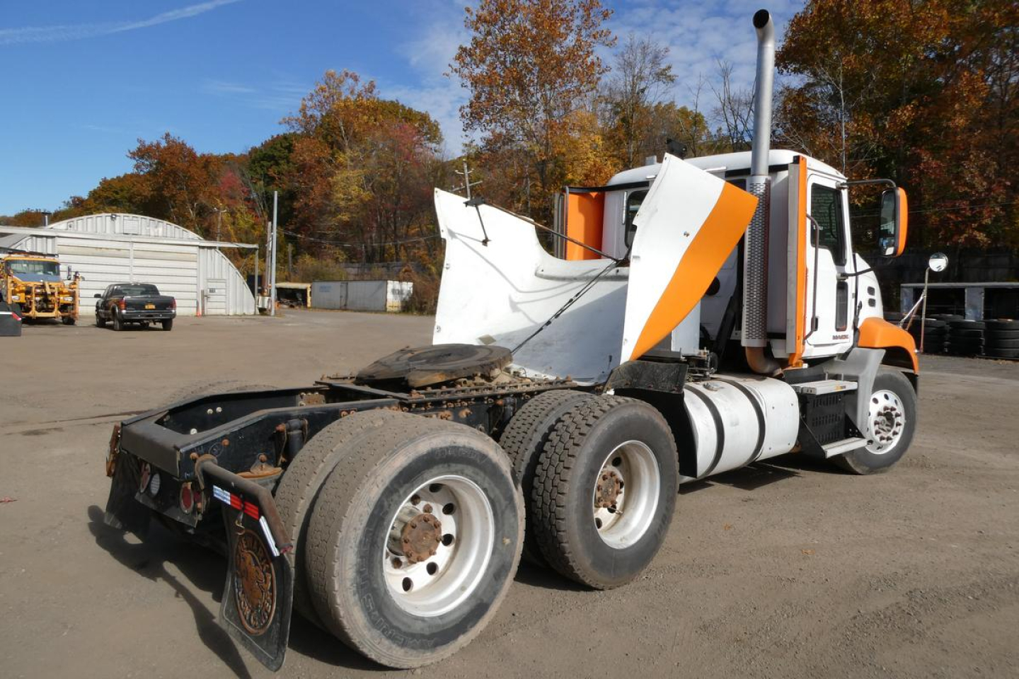 Truck rear three-quarter view showing CXU613 Pinnacle spec with orange and white cab, rear dual axle, fuel tanks, and exposed chassis.
