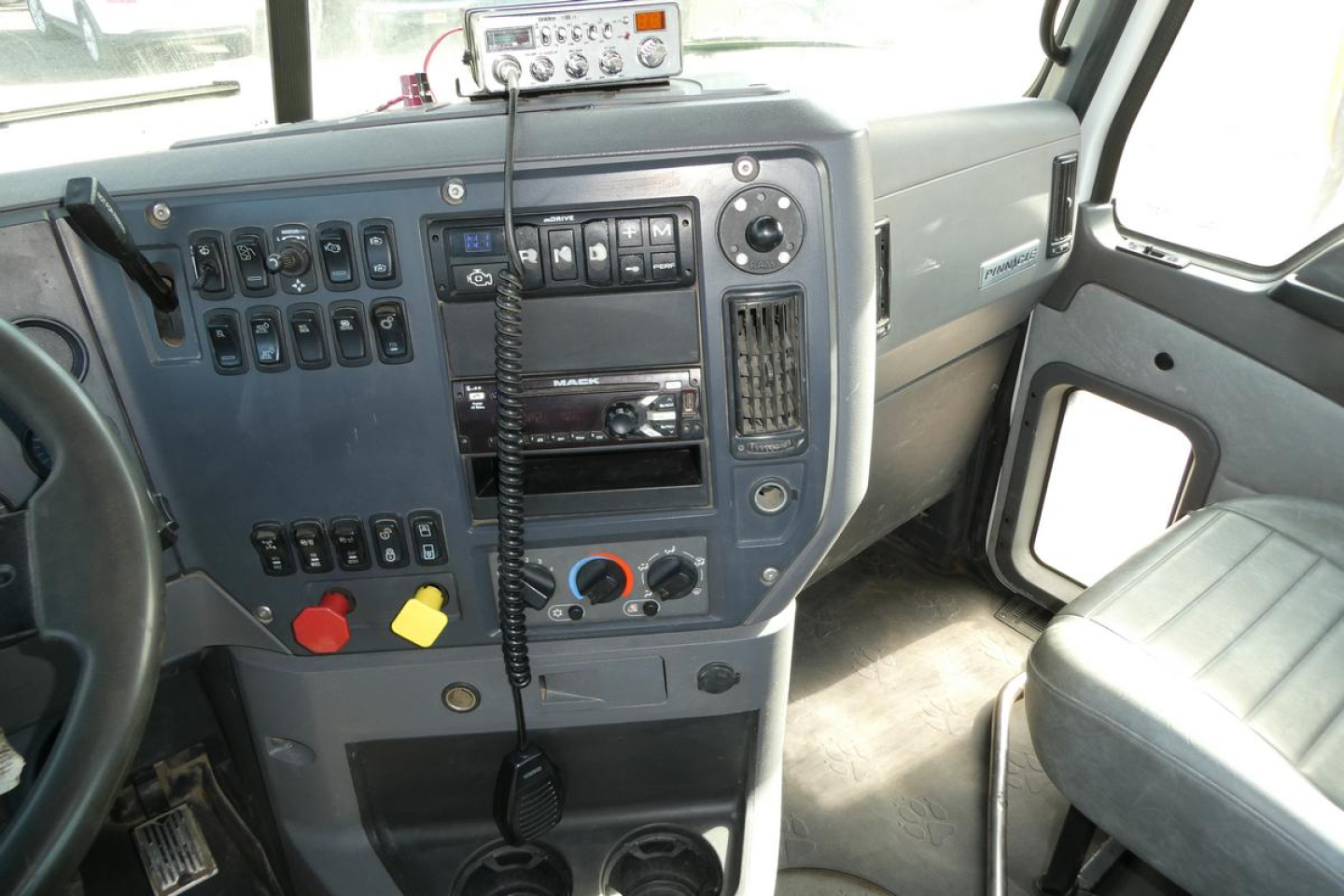 Dashboard of a Mack CXU/Pinnacle truck cab showing control switches, radio, and steering wheel with a microphone.