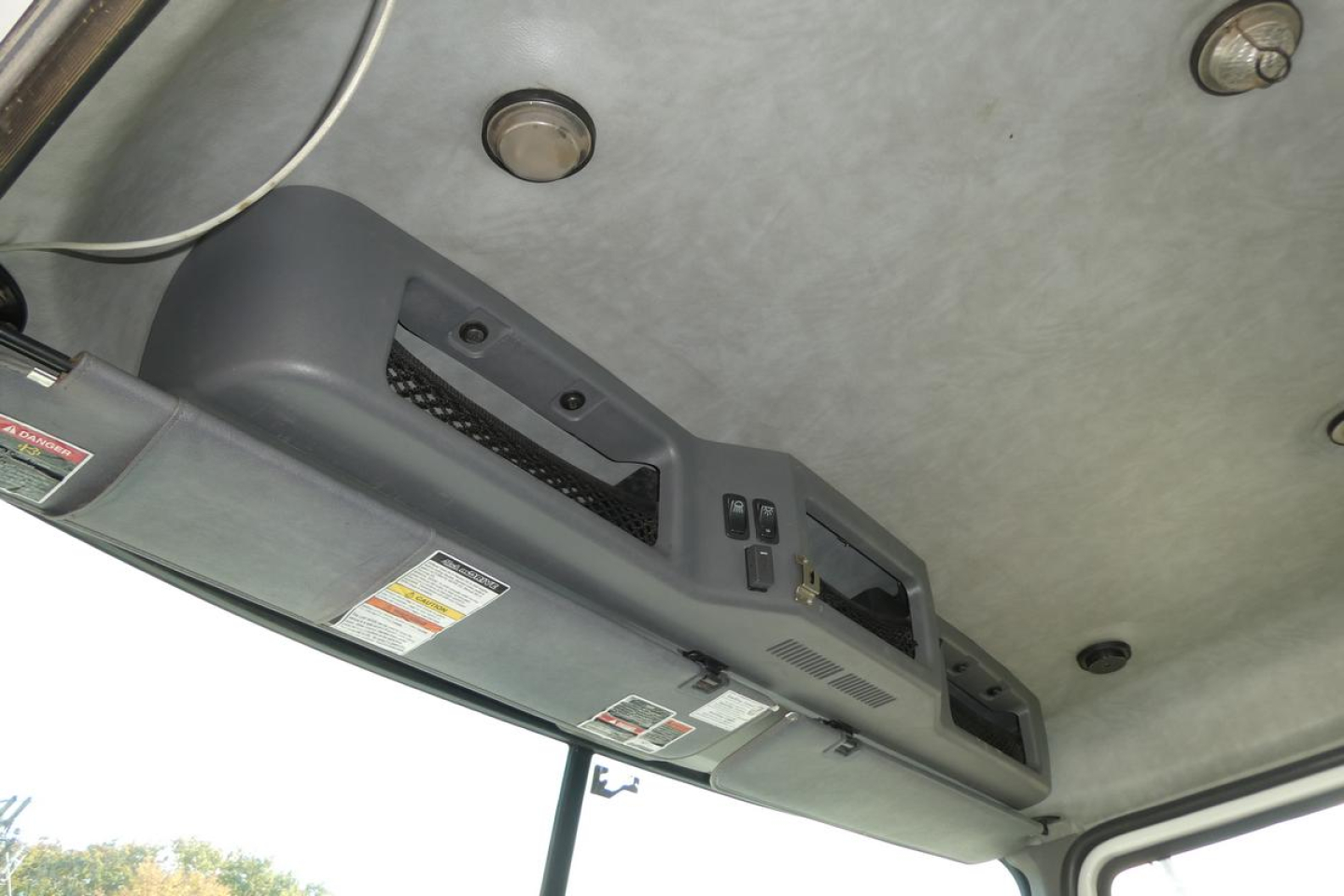 Cab interior ceiling with control panel and vents in a Mack CXU Pinnacle truck cabin. Visible are overhead console with switches and warning labels.