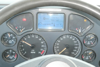 Dashboard view of a Mack CXU truck cab showing tachometers, speedometer, digital display, and gauges in a steering-wheel perspective.