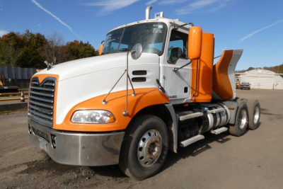 Truck cab showing white and orange Mack CXU pinnacle daycab with front chrome bumper and dual fuel tanks