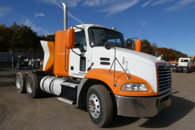 White and orange Mack CXU613 daycab tractor front-right view showing cab and tank, with text on windshield and chrome bumper.
