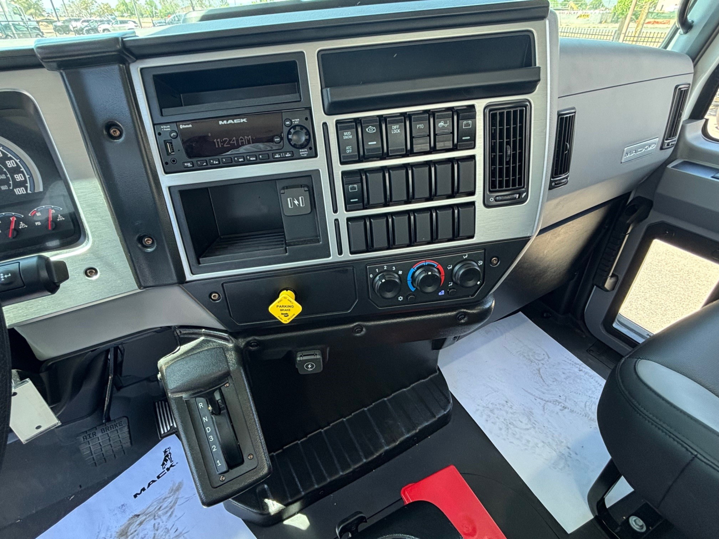 Dashboard and center console of a new 2026 Mack MD6 tractor with multiple switches, radio, climate controls, and a paper document on the passenger side.