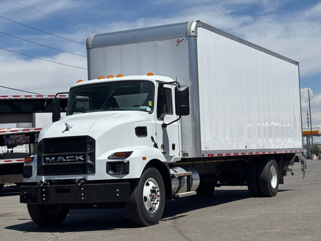 Box truck, white Mack MD6 cab with large rectangular box trailer, front view angled to left, clear sky, dealership lot.