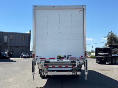 Rear view of a new 2026 Mack MD6 box truck with closed cargo area, rear underride guard, and stabilizing legs extended. VIN tag not visible.