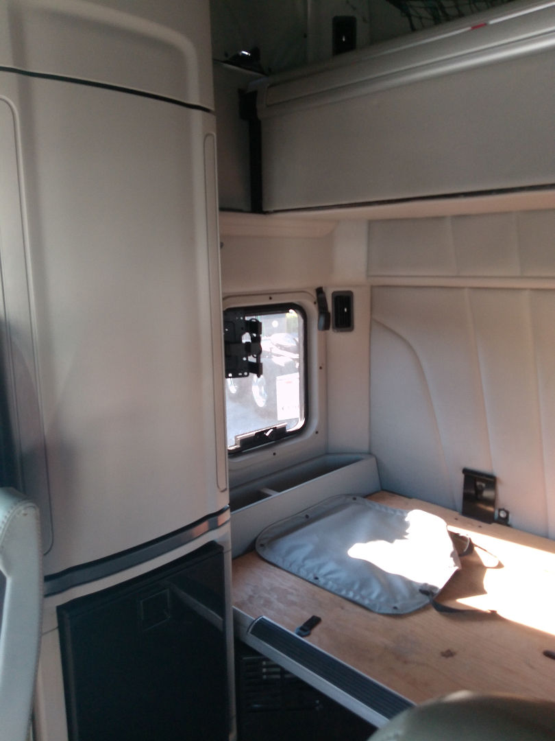 Cab interior of a Peterbilt 579 sleeper showing cabin wall panels and a wooden sleeper shelf with a window and storage area.