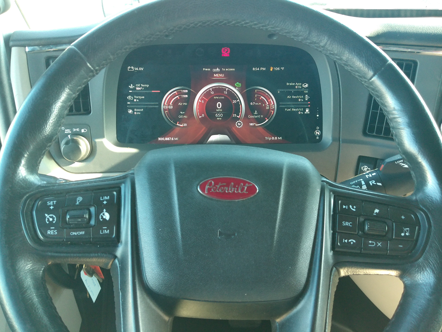 Peterbilt 579 dashboard and steering wheel with digital gauges visible, steering wheel badge center reads Peterbilt, various controls on left and right stalks.