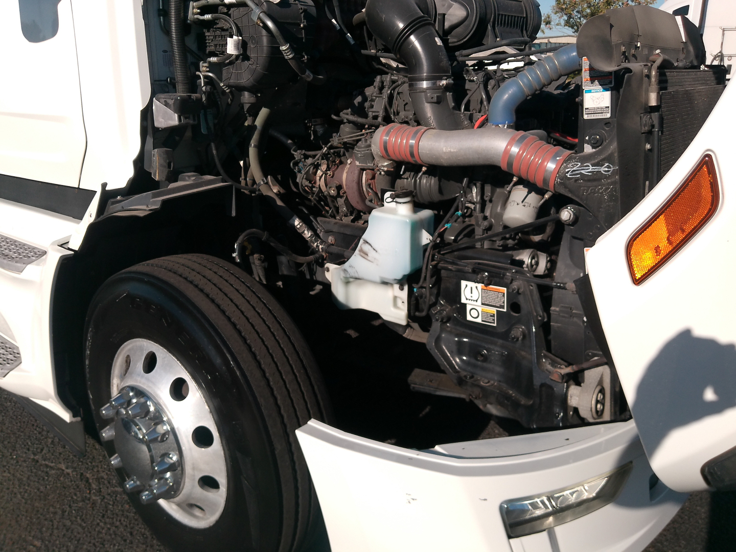 Peterbilt 579 engine bay showing intake hoses, coolant reservoir, radiator, and front wheel with hubcap.
